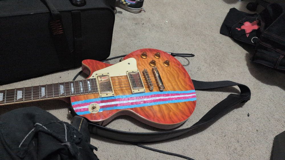 A red electric guitar with a trans flag painted on it 