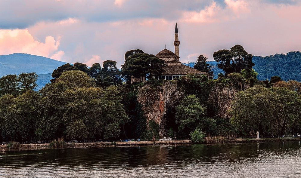 Eine Moschee mit schlankem Minarett thront malerisch auf einer bewaldeten Halbinsel am See von Ioannina, während die griechischen Berge im Hintergrund dezent daran erinnern, dass wir eigentlich in Griechenland sind. Hier verschmelzen osmanische Architektur und mediterrane Landschaft zu einem Postkartenmotiv, das geografisch etwas verwirrt wirkt, aber trotzdem wunderschön ist.