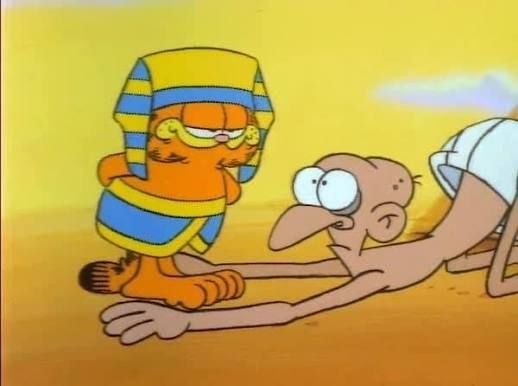 A fat cat dressed as a pharaoh is worshipped by a bald guy on his knees. Desert environment during daylight. Cartoon.