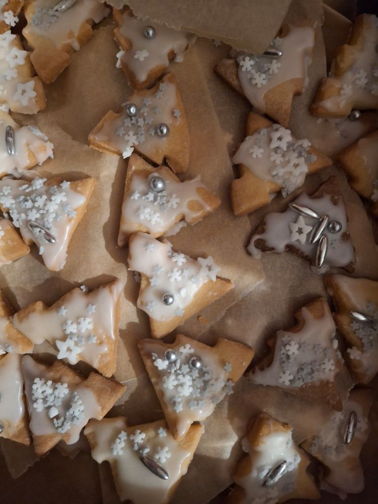 Ca 20 mit Deko in Form silberner Perlen und weißem Schnee verzierte Mürbeteigkekse in Form von dreieckigen Bäumen.