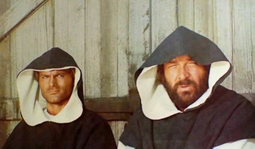 Zwei kräftige, entschlossen wirkende Mönche sitzen vor einer Holzwand. Foto aus einem Bud Spencer Film.