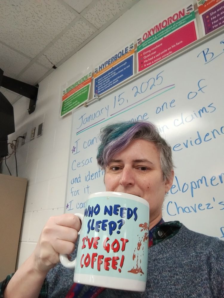 A very tired teacher holding a giant coffee mug that says, "Who needs sleep? I've got coffee."