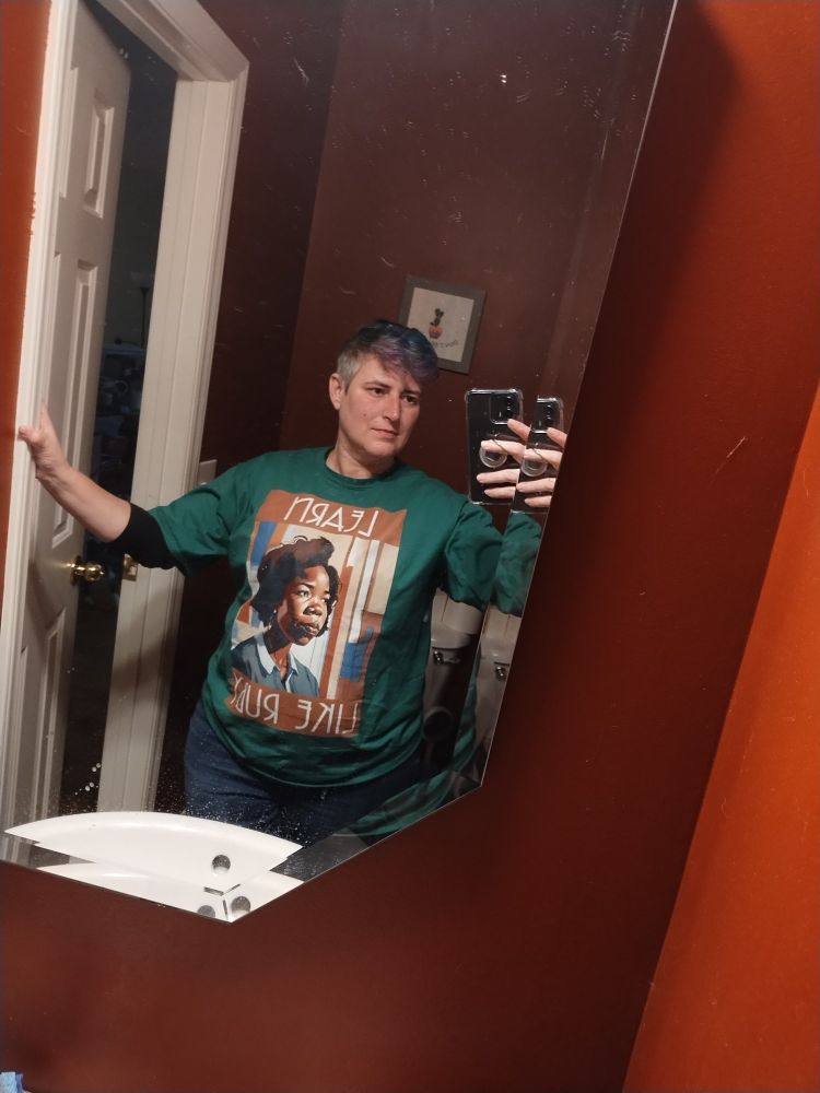 Woman wearing a green t-shirt with a drawn version of Ruby Bridge's face as a child, that says, "Learn Like Ruby."