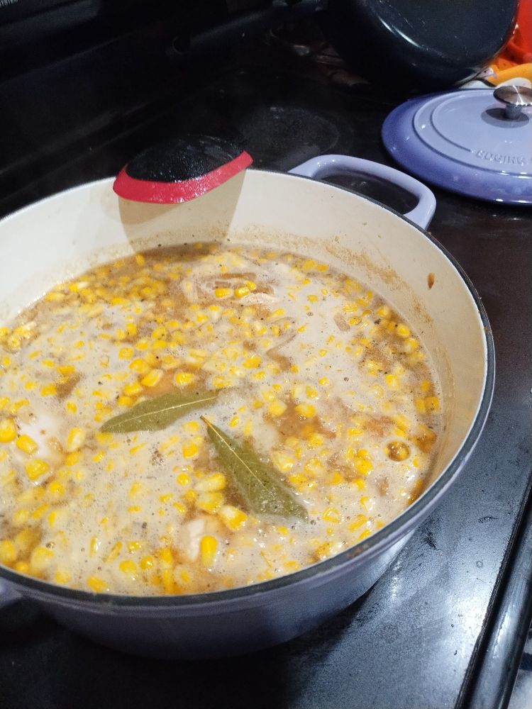 Large Dutch oven filled with white chili with corn and two bay leaves visible.