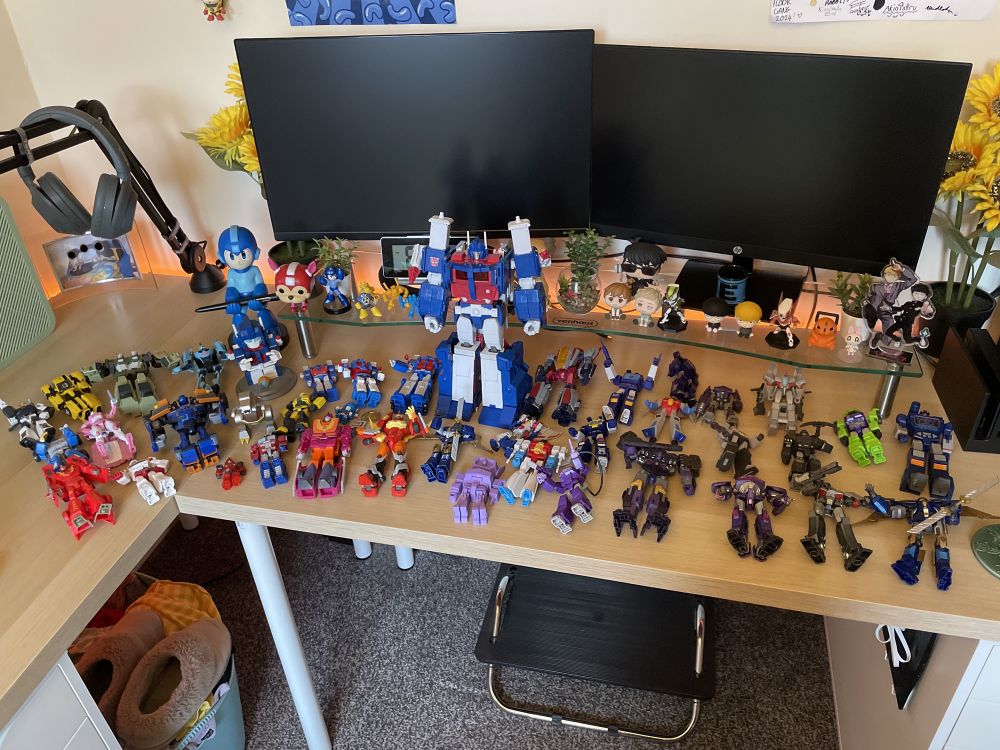 Multiple Transformers figures laid out on a desk after being dusted. They are all laying down, except for a large Ultra Magnus who stands amongst the carnage