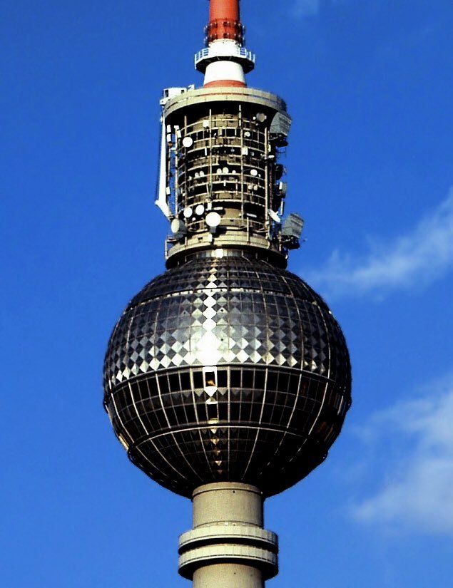 Das Foto zeigt die Kugel des Berliner Fernsehturms. Auf der metallischen Oberfläche spiegelt sich die Sonne. Dies sieht aus wie ein Kreuz