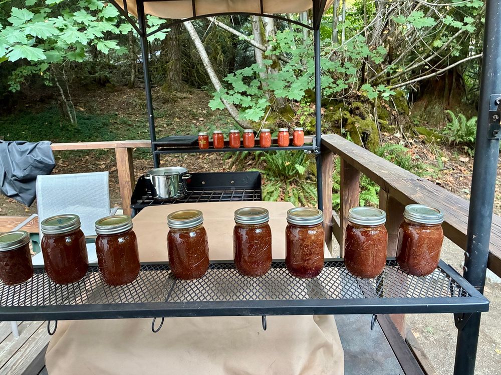 In the outdoor kitchen: Jars of plum jam in the foreground and jars of tomato sauce in the background.