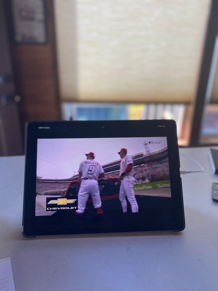 ipad showing the broadcast of the bristol racetrack mlb pre-game of two bball players waving to crowd from back of pickup truck circling on racetrack