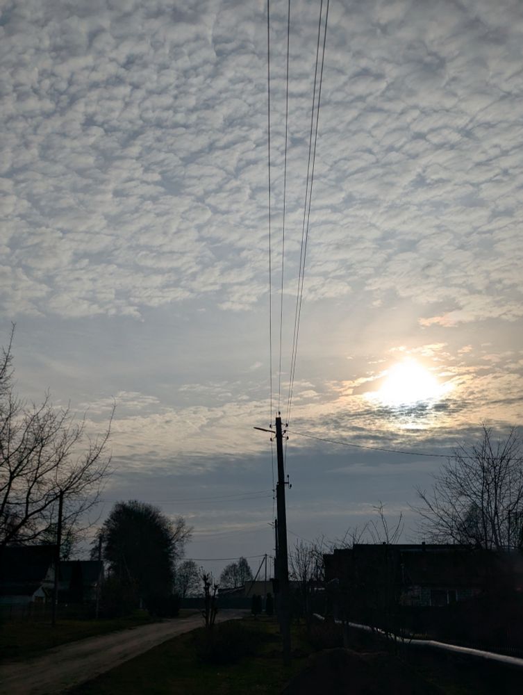 Ранішняе сонца сярод лёгкіх аблокаў над вясковымі дахамі.