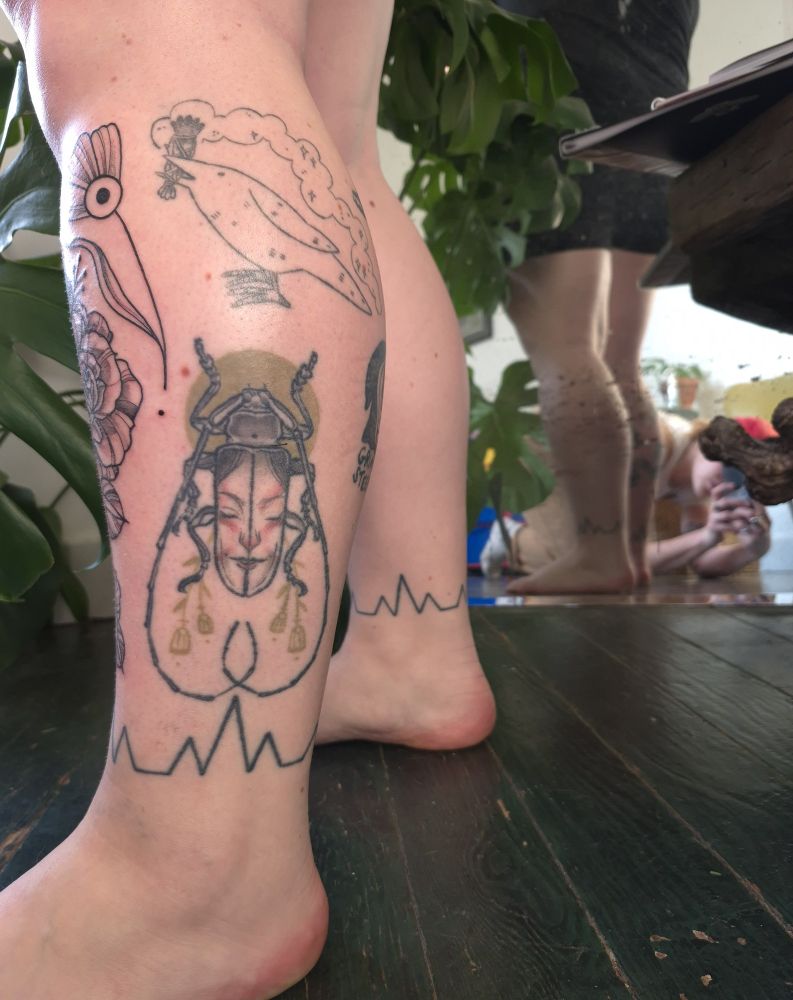 Healed coloured beetle tattoo with face in the wings on lower leg surrounded by other flash 