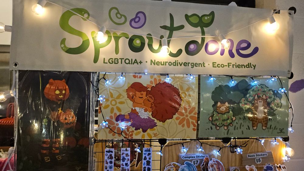 The top half of the Sproutdone booth showing large poster size art prints.  Includes a plant cat design, a pumpkin witch design, and a sapphic design.