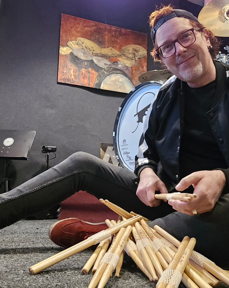 Ein Schlagzeuger sitzt auf dem Boden mit einer Lieferung Drumsticks.