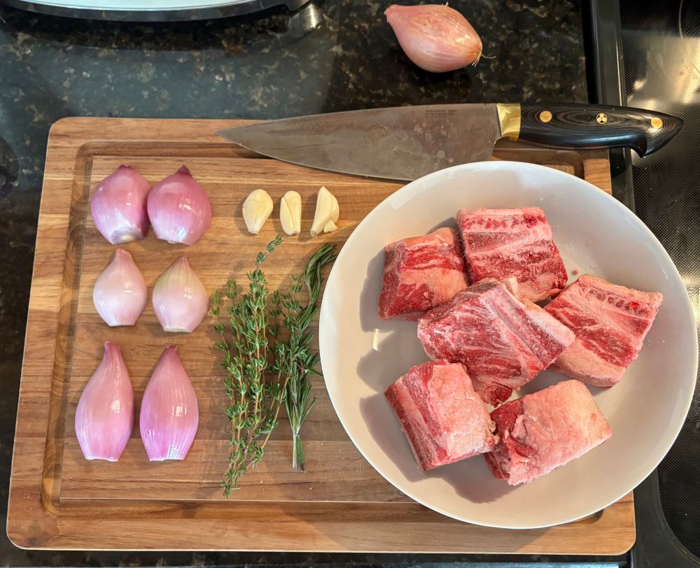 Cutting board with prepped shallots, garlic, herbs, and beef short ribs 