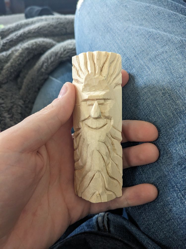 A face with wild hair and beard carved into a small block of wood about 4 inches tall.