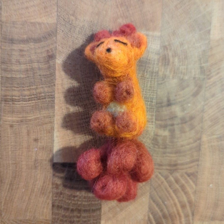 Needlefelted Vulpix, sleeping on their back, with wooden background 