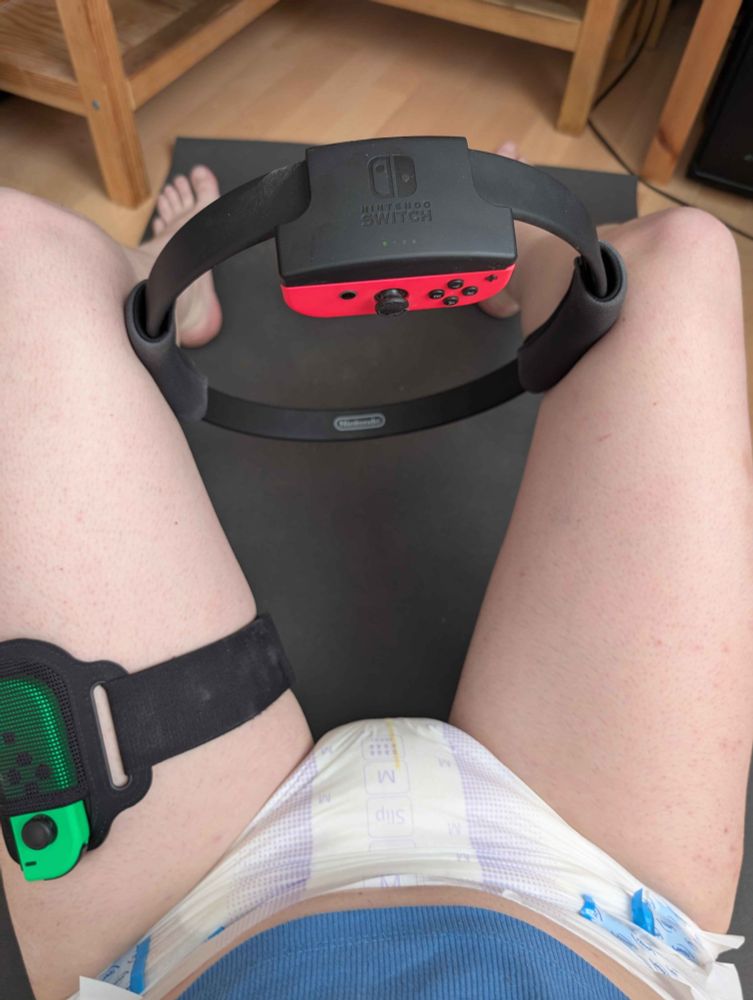 A photo of my lower body, wearing a blue crop top and a (for now) dry Tena Maxi diaper. I'm sitting on a yoga mat doing the "thigh" press exercise.