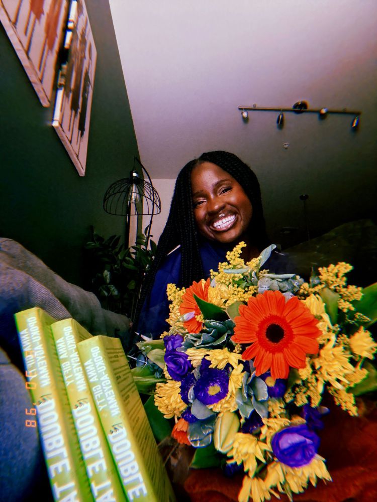 ANNA THE AUTHOR WITH THE BOOKS SHE WROTE AND SOME COLORFUL FLOWERS