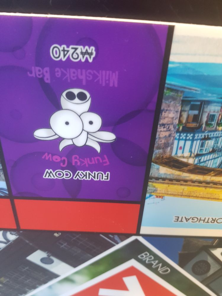 a photo of a monopoly space from the monopoly chester board, showing the "Funky Cow" space, including the logo for funky cow which is a cartoon depiction of a cow with big eyes. it is upside down, resembling what the post labels it as