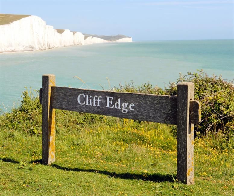 Image shows cliff edge sign with view of Seven Sister cliffs