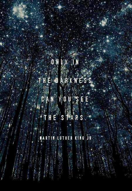 Dark trees and night sky.. lit up by some bright stars. Quote says: Only in the darkness can you see the stars. .Martin Luther King.
