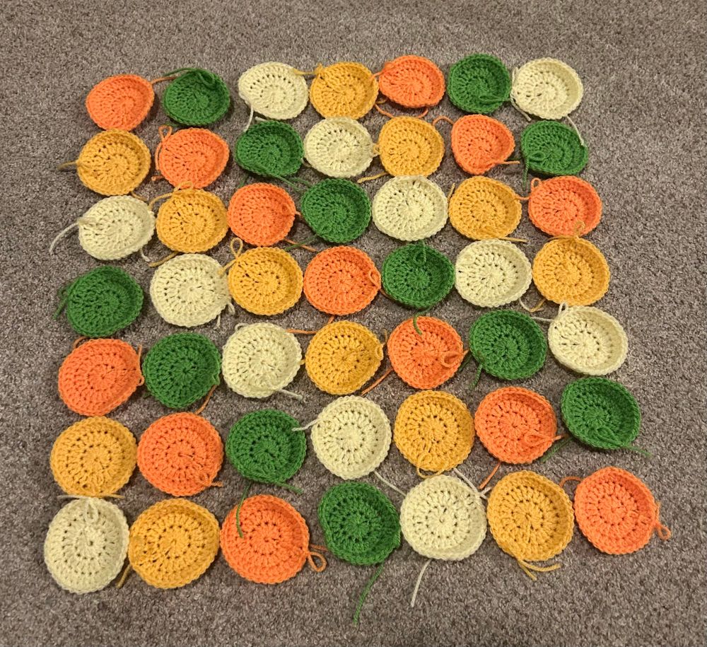 Yellow, light orange, less light orange, green crocheted dots in a 7x7 square pattern 