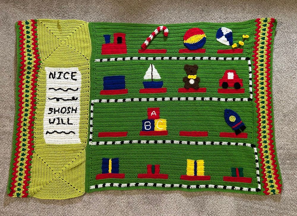 Crochet blanket, left and right side has an ugly sweater zig zag border, on the left is a swath with a nice list, most of it is a darker green with the start of a train with different tracks having toys like a train, candy cane, ball, kite, box that will be a drum, boat, teddy bear, car, abc blocks, rocket, presents. 🧶 4/6 done, 2 weeks to go 