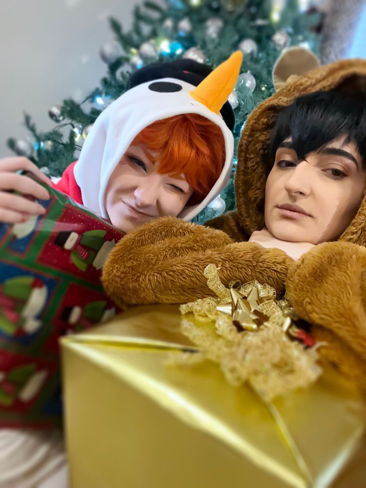 Tobio Kageyama and Shoyo Hinata, Haikyuu, in snowman and reindeer onesies. They are holding Christmas presents and are infront of a Christmas tree for the holidays. This is cosplay.