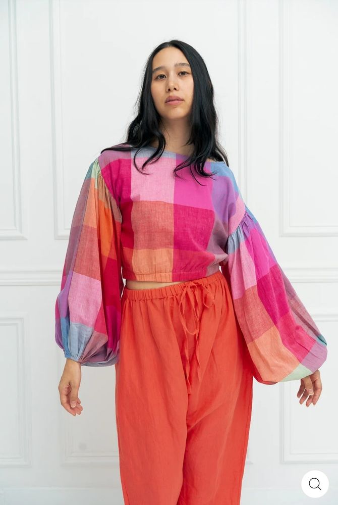 Une dame qui pose avec un haut à carreaux roses, verts, oranges et bleus