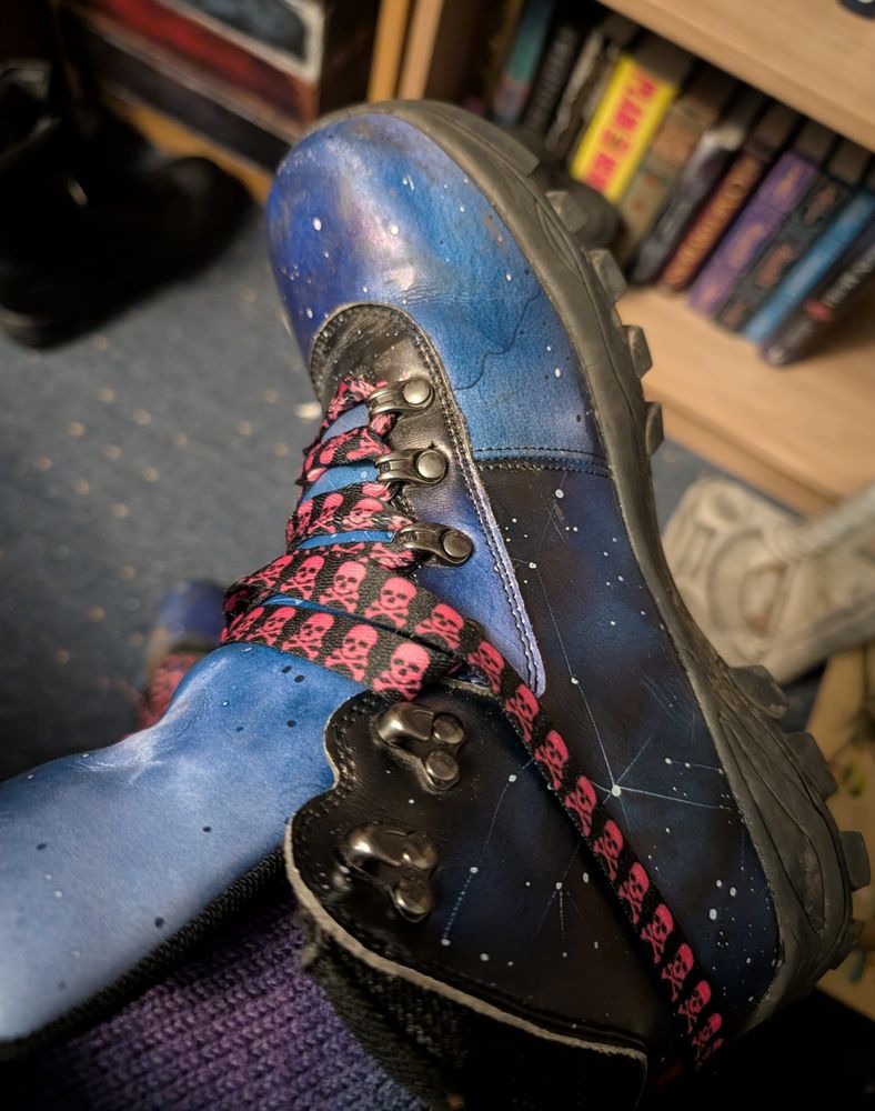 A boot, patterned after a starry sky, with black laces adorned with pink skull and crossbones.