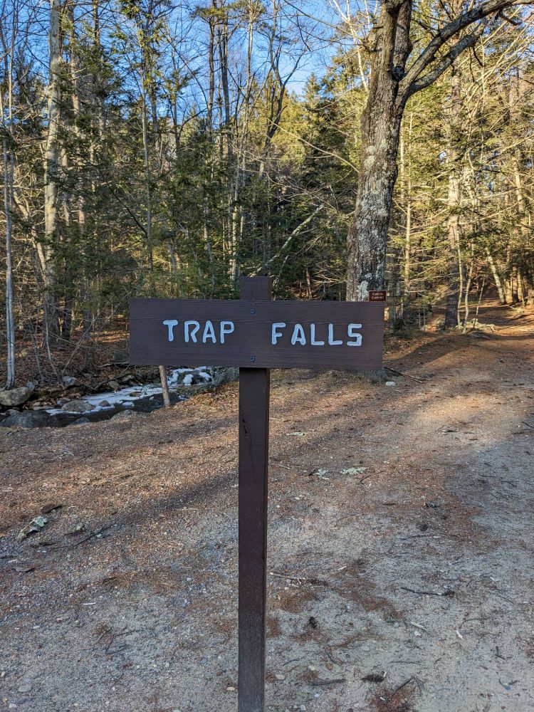 A sign saying 'Trap Falls,' in front of a background of trees 