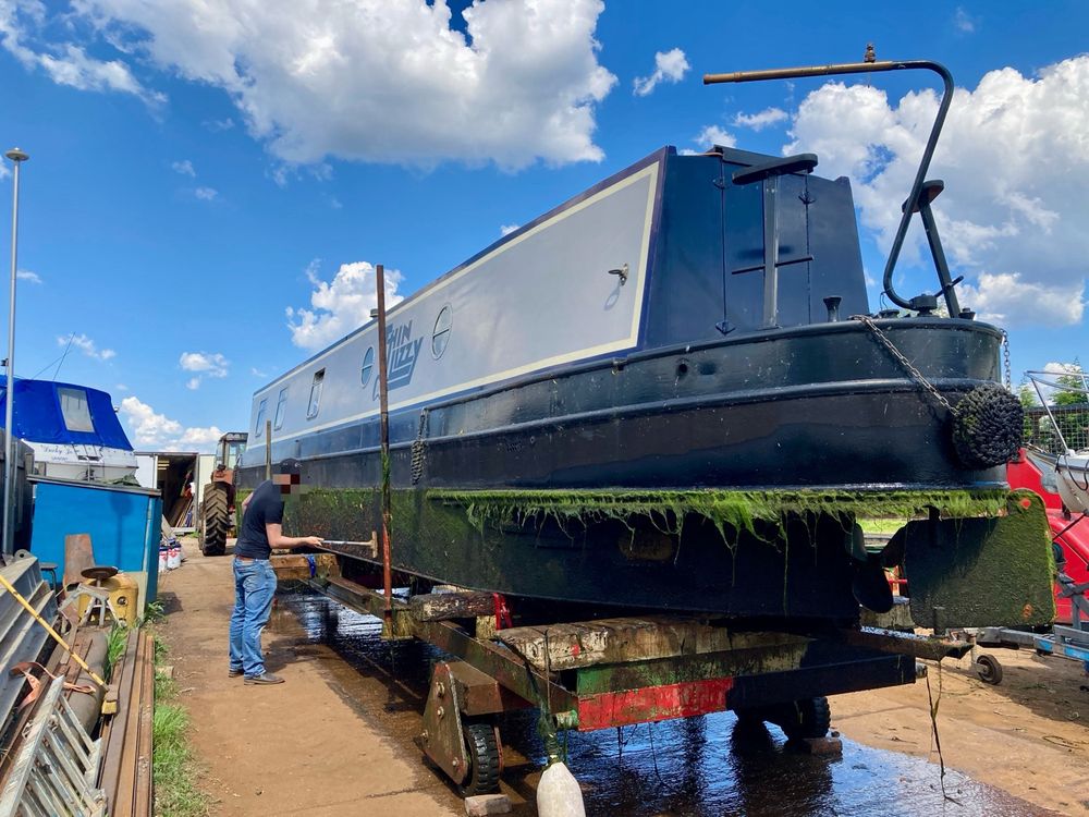 Grey and black narrowboat on slipway being prepared for hull painting 