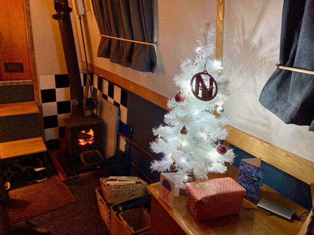 Little white Christmas tree lit up inside a cosy narrowboat 