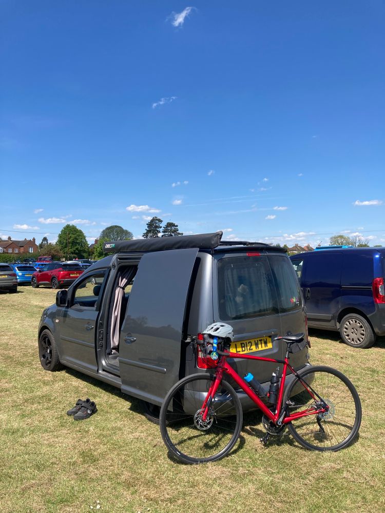 Grey vw van and red road bike in a field 