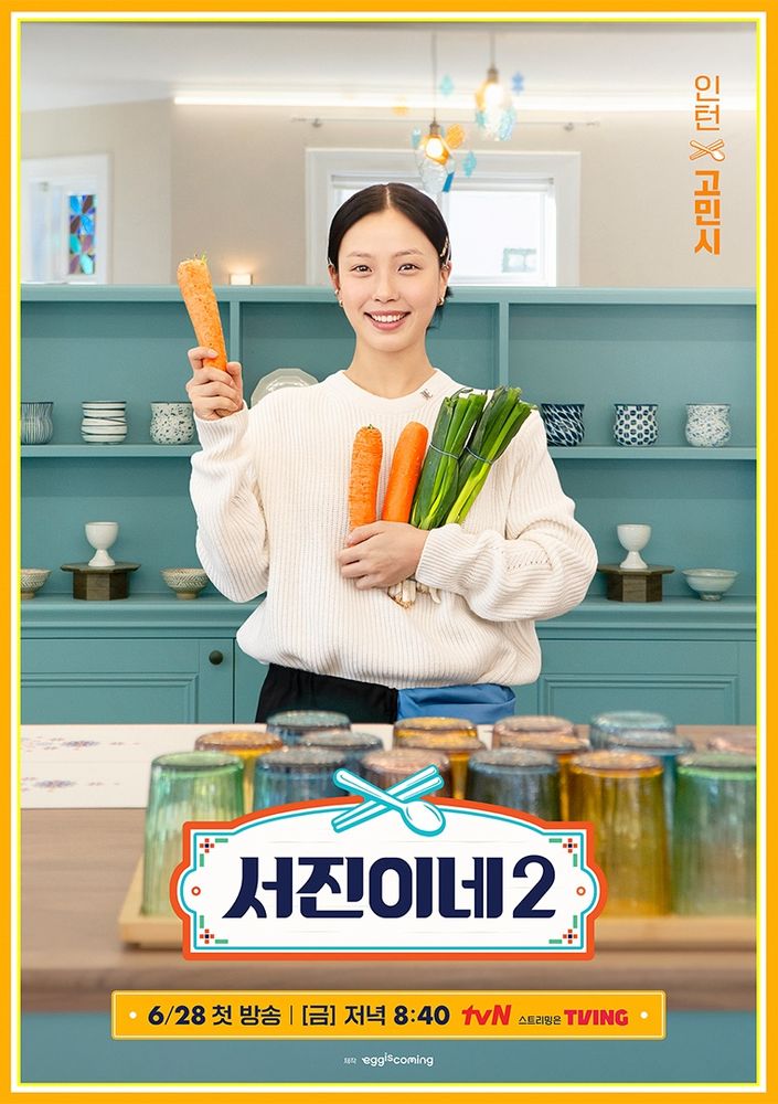 In a promotional poster for the Korean reality cooking travel show Jinny's Kitchen Season 2, Go Minsi stands in a kitchen set, holding carrots and green onions. A big smile is on her face. She is holding up one carrot in her right hand. 
