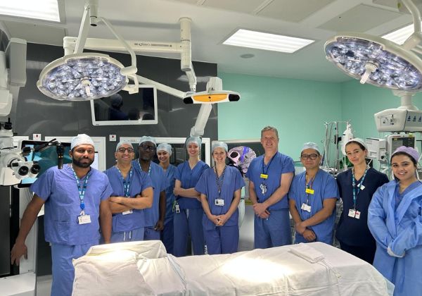 A group of healthcare professionals in scrubs stands together in a modern operating room, surrounded by medical equipment.