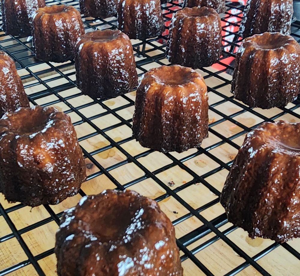 A photo of Canelés cooling on a wire rack. The sheen of the buttery crust is very visible.
