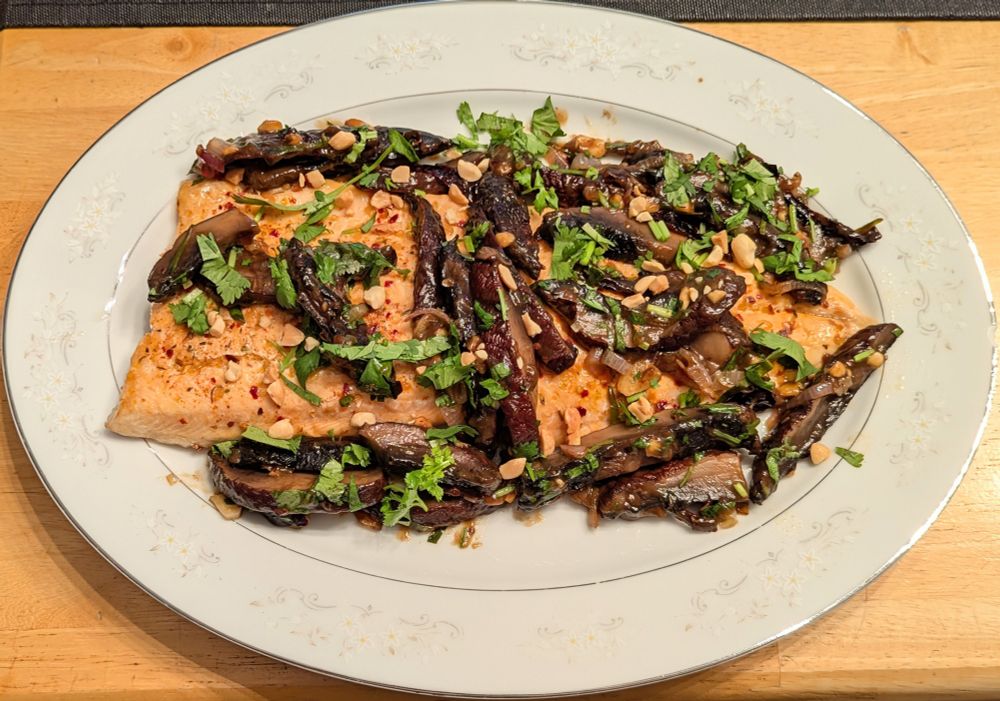 A white oval plate holding a side of roasted arctic char topped with stir fried portobello mushrooms, garnished with cilantro and peanuts 