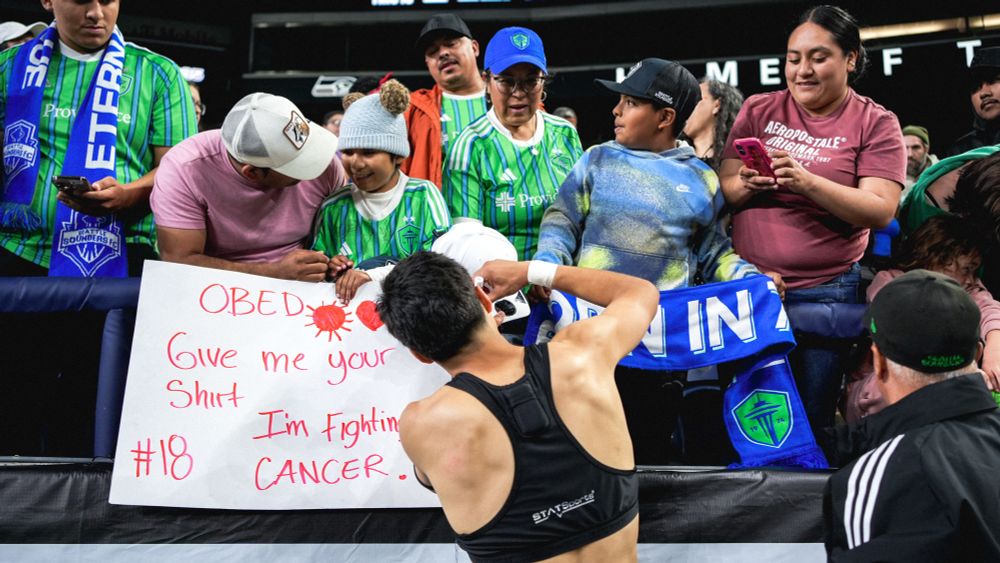 Obed gives jersey to young fan who is holding a sign they are battling cancer