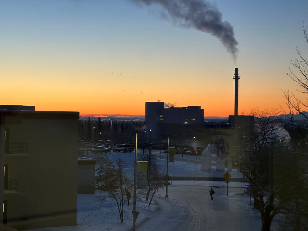 Power plant silhouetted against  sky shading from orange at the horizon to blue at the top