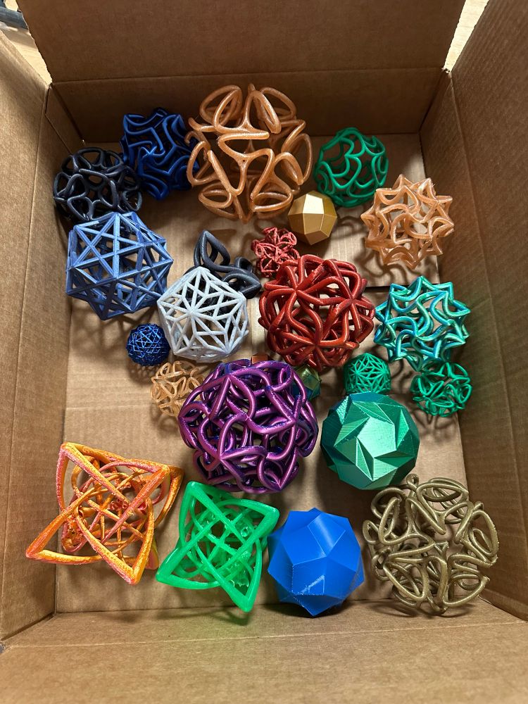 A cardboard box filled with various 3D printed math sculpture in a variety of colors. 