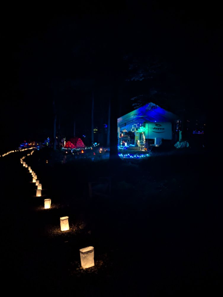 A pathway lined with luminaries in front of a campsite lit with blue and green lights