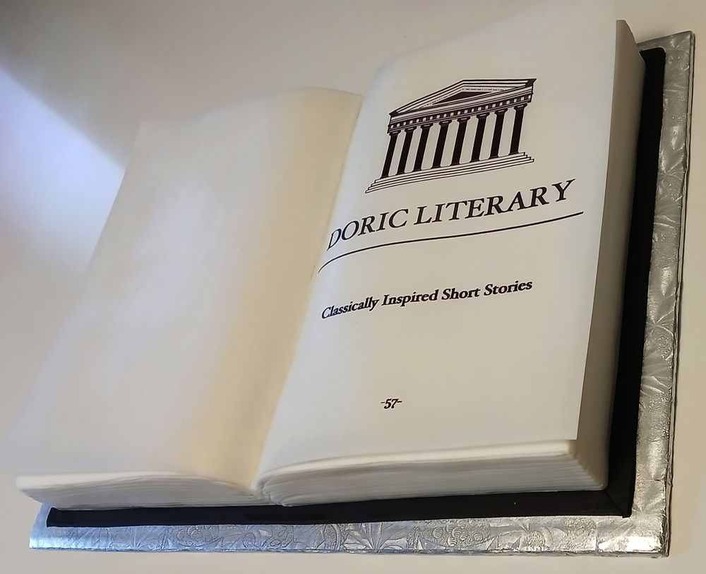 Doric Literary logo on a cake shaped like a book.