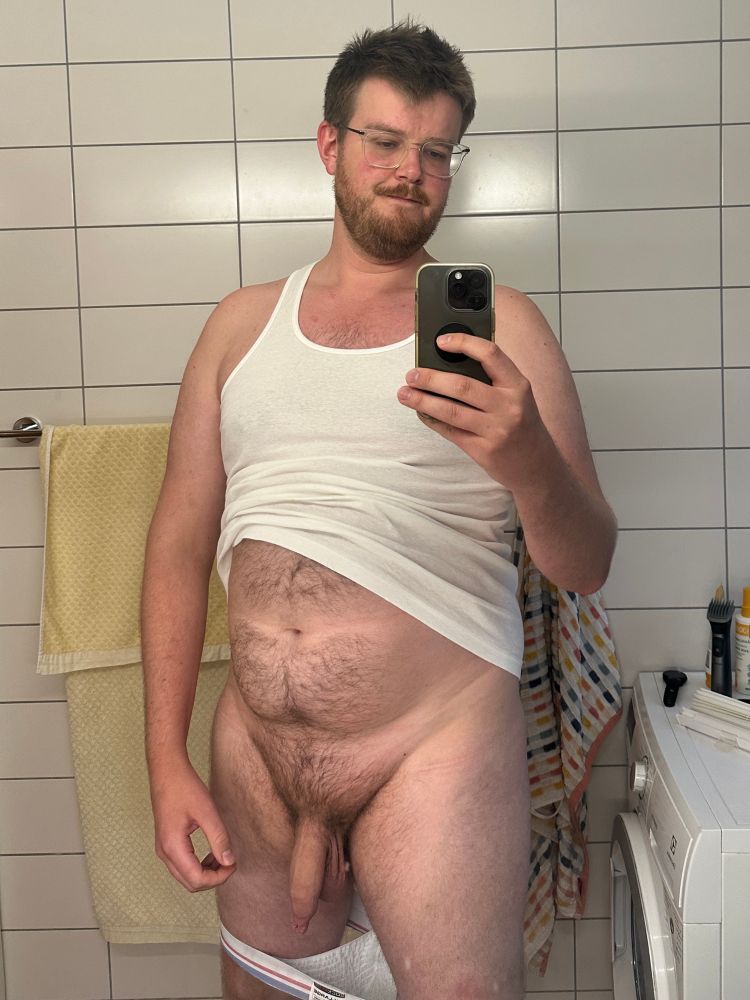 Man wearing a white tank top, lifted slightly showing off belly, with his soft uncut cock out