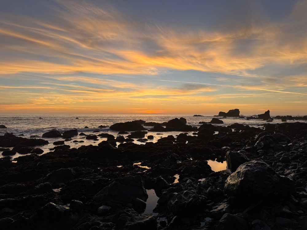 Glorious blue and orange striped sunset over black rocks 