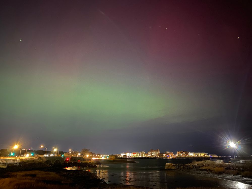 Bright green aurora borealis colors the lower sky and red is visible higher up above the Boston skyline.