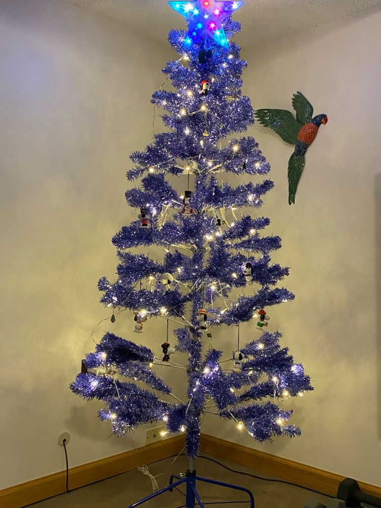 A blue tinsel tree with white lights and a bunch of vintage snoopy ornaments all over it. 