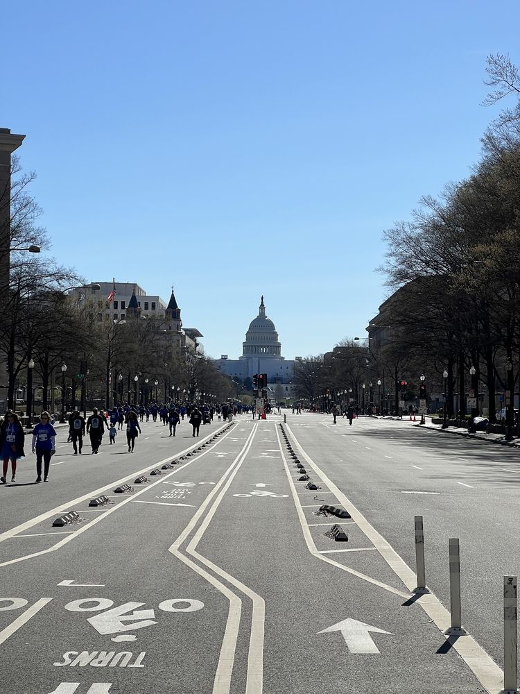 A view down a long road leading to the dome of the US Capitol building The road is closed and runners in blue shirts are coming down one side of the road towards the camera