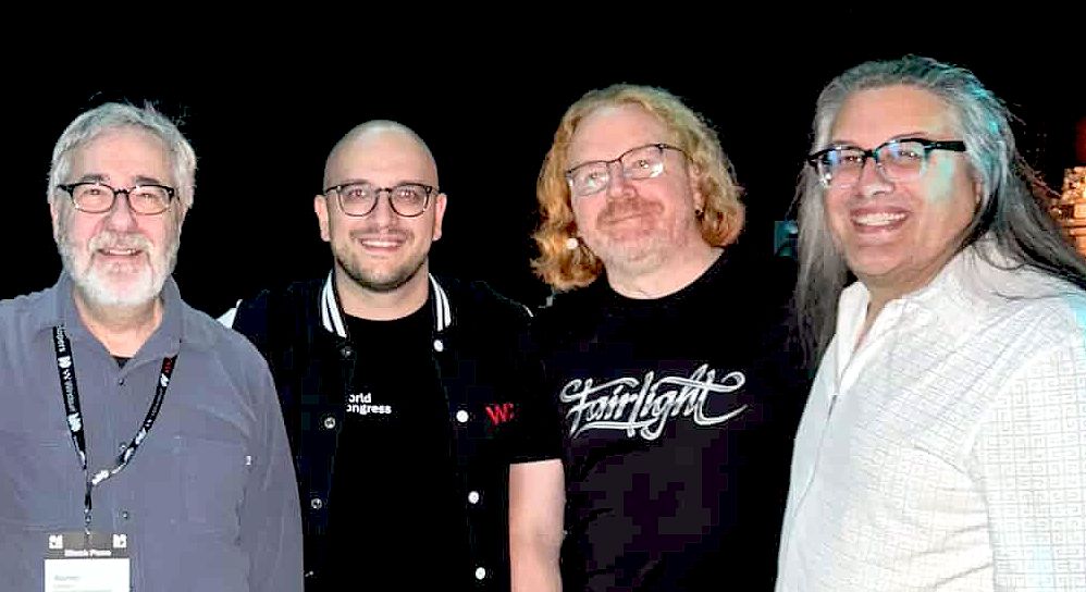 4 people posing for a photo, featuring John Romero and Warren Spector. Christian wears his FairLight t-shirt.