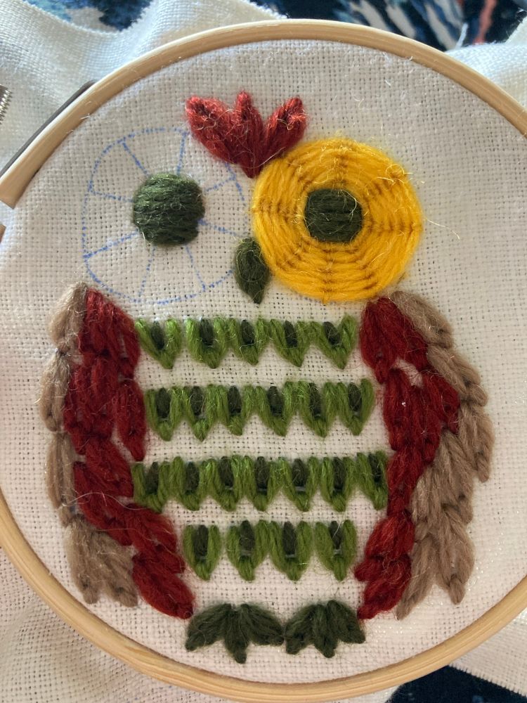 Vintage stylized owl crewel embroidery design in green, rust red, beige, and yellow on white homespun. 