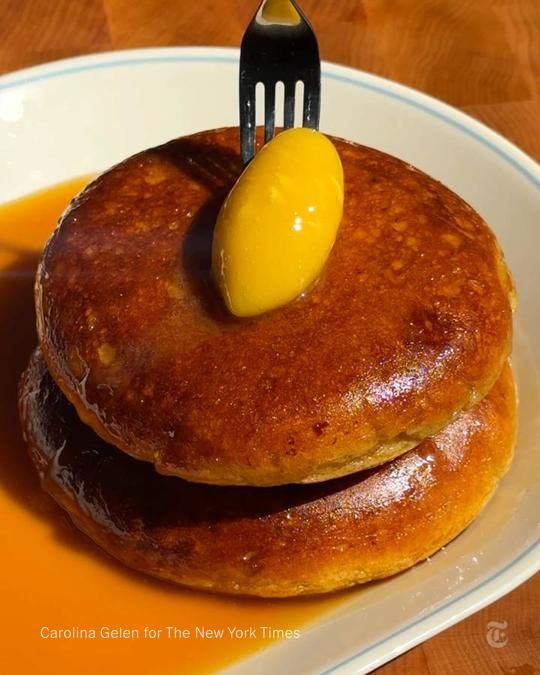 A stack of two thick pancakes in syrup with a dollop of butter on top.